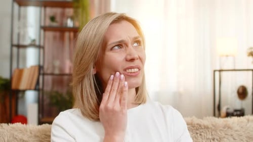 Adult Woman with Toothache at Home Holding Jaw and Showing Pain Expression While Sitting on Sofa