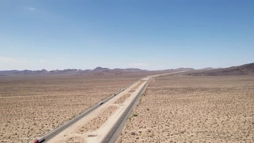 Aerial panoramic view of freeway in desert. Vehicles driving on long distance through arid area. Sun