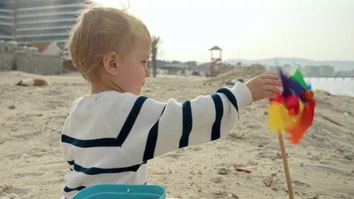 Portrait of little toddler boy playing with spinning colorful pinwheel toy on the sandy sea beach