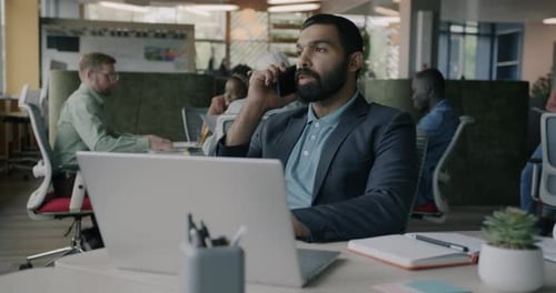 Portrait of Office Worker Speaking on Mobile Phone and Working with Laptop at Desk at Work