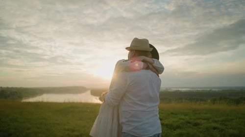 Lovers Embracing in a Field at Sunset with White Outfits and Hats