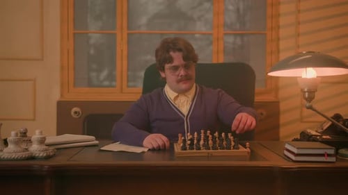 Mann mit Schnurrbart in einem Retro-Büro sitzt an einem großen Tisch und arrangiert Schachfiguren auf dem Brett