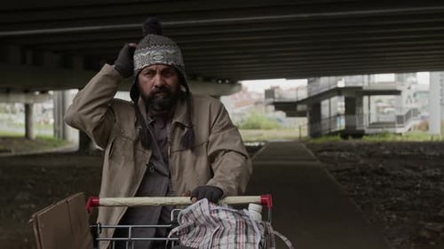 Portrait of Tottering Middle-Aged Male Vagabond Scratching Head under Bridge