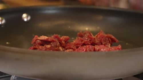 Stir frying slices strips of skirt or flank steak in a pan or wok with oil on the gas stove - close