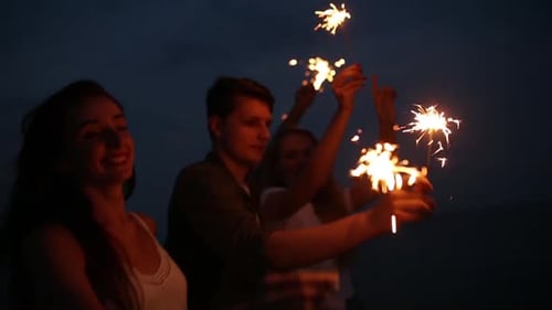 Amigos caminhando, dançando e se divertindo durante a festa noturna à beira-mar com luzes cintilantes de Bengala