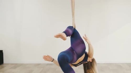 Portrait of Young Blonde Fit Woman Doing Aerial Yoga Exercise on Hammock in Yoga Studio