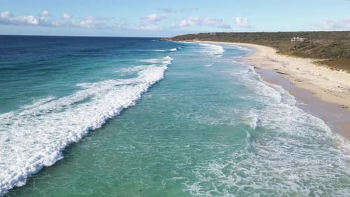Aerial flight along a sunny beach with waves crashing on the sand