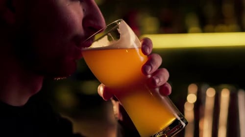 Gros plan sur une table de bar en bois, un gars boit dans un verre de bière légère, éclairage chaud