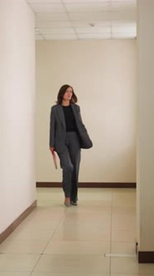 Businesswoman Walking Through Office Hallway Holding Red Notebook