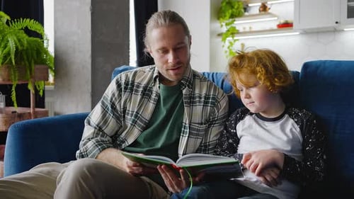 Man Reads a Book to Curly-Haired Child Indoors