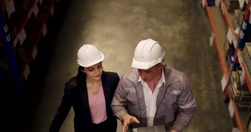 Warehouse manager pair reviews cargo strategy while standing beside packages and using laptop during