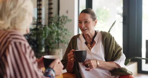 Two Senior Women Chatting and Drinking Coffee Indoors