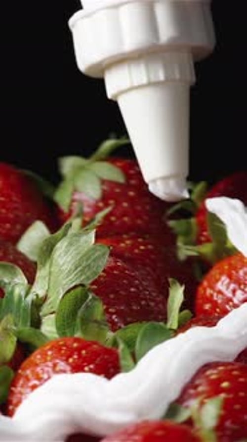 La crema batida se exprime de una manga pastelera sobre fresas giratorias sobre un fondo negro.