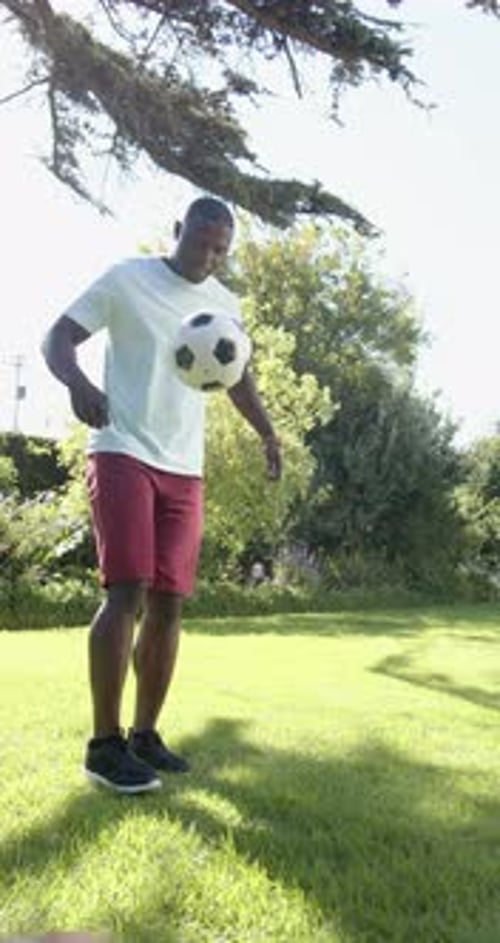 Vertical video: Man playing soccer in sunny park, focusing on ball control and technique