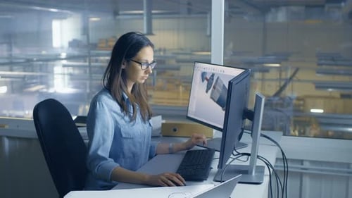 Female Industrial Engineer Works on Her Computer with CAD 3D Software. Inside of the Factory is See