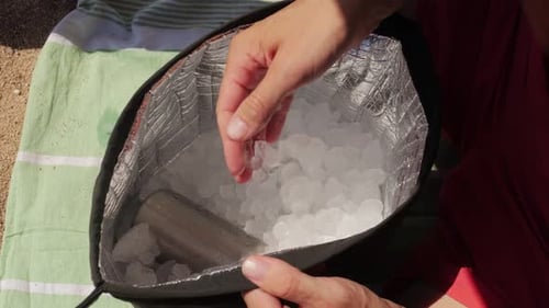 A Pair of Hands Gently Holding Ice Cubes Taken From a Bag Resting on a Green Towel