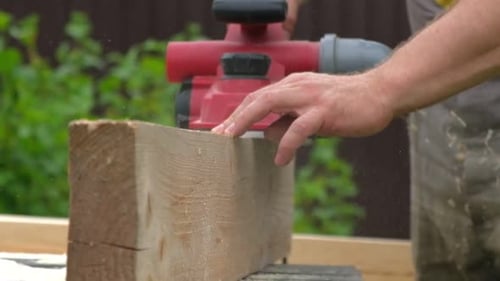Male Carpenter Using Electric Circular Saw in Backyard Workshop with Wood Chips Flying Building