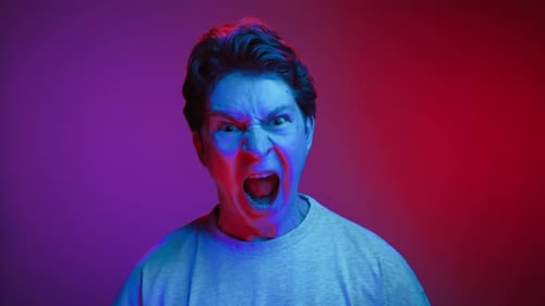 Portrait of Young Man Looking at Camera and Screaming in Neon Lighting of Studio