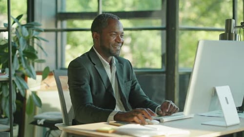 Close Up Attractive African American Man Working on the Computer Smiling in the Office at His Desk
