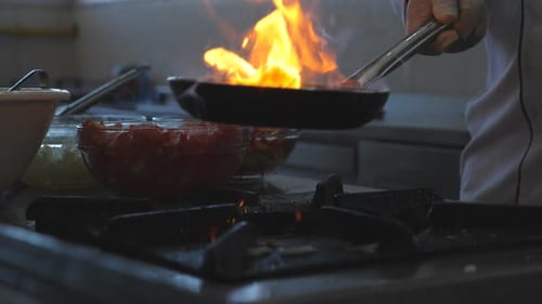 Detail View on Flaming Pan in Hand of Professional Chef Cooking Tasty Flambe Style Dish Professional