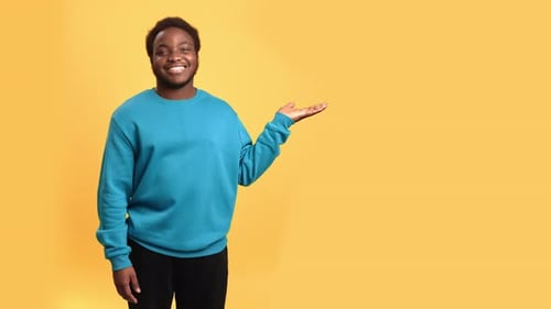 Smiling African Man Posing with Pointing Hand Gesture Showing Copy Space Isolated on Orange Studio