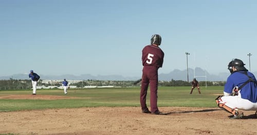 Playing baseball, batter in maroon uniform preparing to hit pitched ball