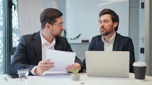 Businessmen Talking About Paperwork at Desk in Office