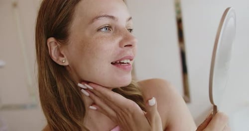 Woman Checks Face in Handheld Mirror Indoors