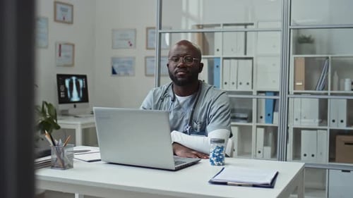 Doctor in Scrubs Sits at Desk in Office