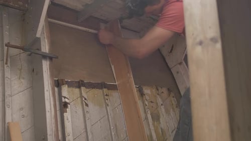 Um jovem carpinteiro desenhando o interior de madeira compensada de um barco de madeira