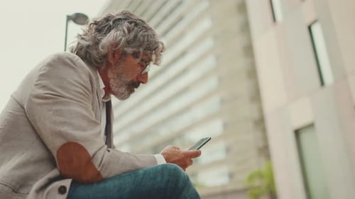 Profile of mature businessman wearing gray jacket is using cell phone