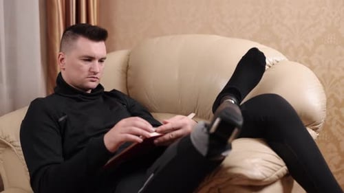 Man Reads on Cream Couch in Black Sportswear