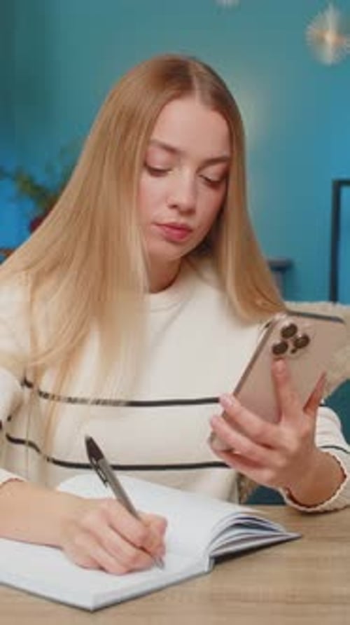 Young Woman Takes Notes While Looking at Phone