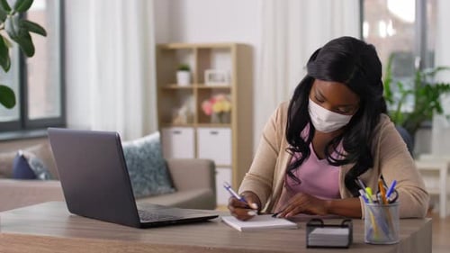 African american woman protected by medical mask works from home during pandemic