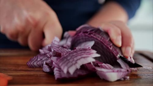 Close up of a woman cutting up a red onion near other vegetables on a wooden cutting board