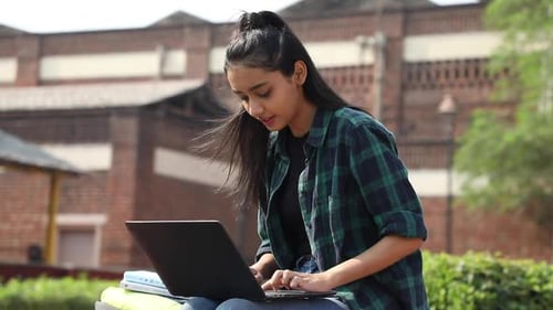 Video of an Indian college girl sitting on a university campus, working on a laptop.