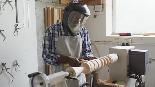 African american male carpenter wearing protective helmet turning wood on a lathe at carpentry shop