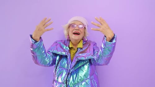 A Smiling Cheerful Elderly Lady Poses in Front of the Camera on an Isolated Purple Background