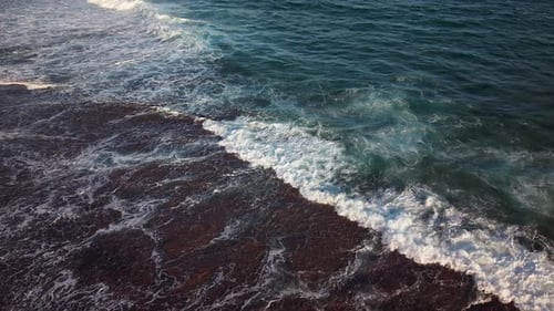 Aerial Drone View of Powerful Ocean Waves Crashing on a Dark Volcanic Rocky Shore in Slow Motion