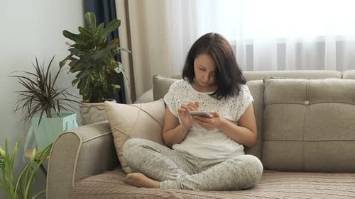 Woman Relaxing on Couch Using Smartphone Indoors