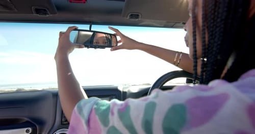 Young African American woman adjusts the rearview mirror in her car on a road trip