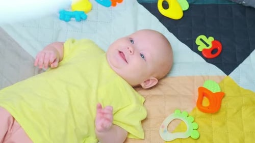 Cute Little Newborn Baby Surrounded By Colorful Toys Lying at Home on the Bed
