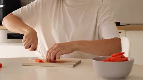 Close up of a woman slicing fresh carrots on a wooden cutting board in a contemporary kitchen.