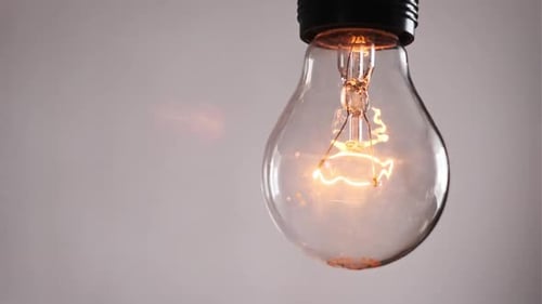 Lightbulb Filament Illuminates on Soft Gray Background