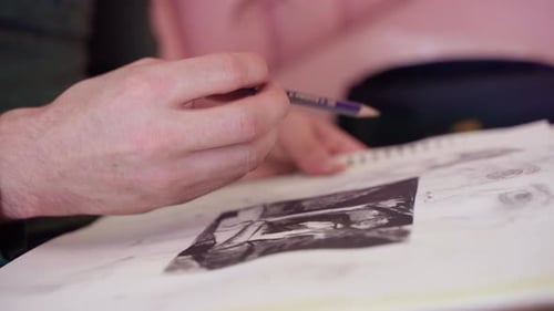 Extreme close up profile shot of artist's hand drawing picture on sketch pad with graphite pencil