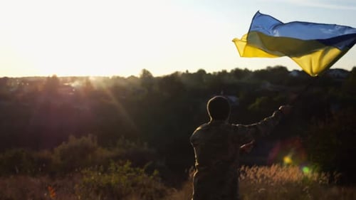 Ukrainian Army Man Waving National Banner Against Background of Sunset Young Male Soldier Lifted