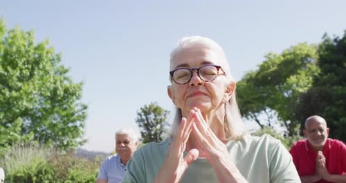 Senior caucasian woman practicing yoga meditation with diverse senior group in garden, slow motion
