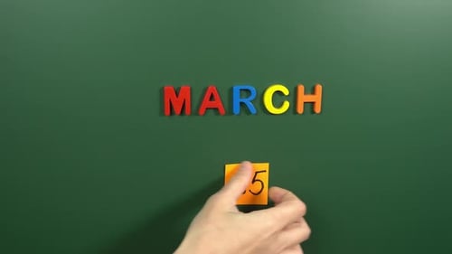 Hand sticking a sticker 25 March calendar day on school board. 25 date of March. Twenty fifth day