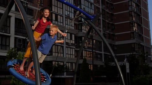 Little Boy and Girl Ride Together on a Swing in a Modern Yard and Playground