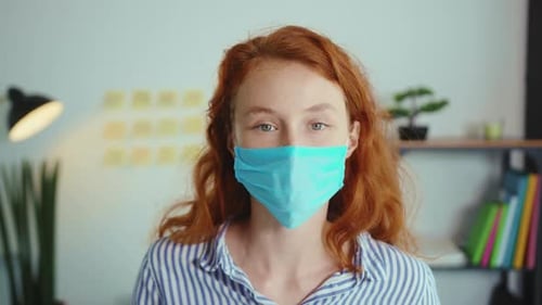 Close Up Smiling Woman Employee in a Medical Facial Mask Works in the Office Look at Camera